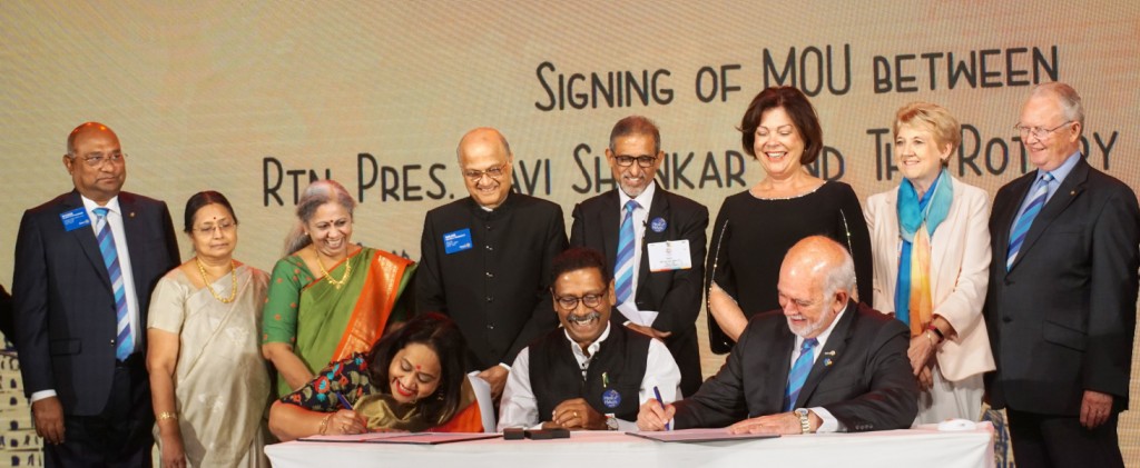 RI President Barry Rassin signs an MoU with RC Bangalore Orchards President Ravi Shankar and spouse Paola in the presence of (from L) RID C Basker, Mala, Anita Hari, TRF Trustee Gulam Vahanvaty, D 3190 DG Suresh Hari, Esther Rassin, Alison Webb and TRF Trustee Mike Webb.