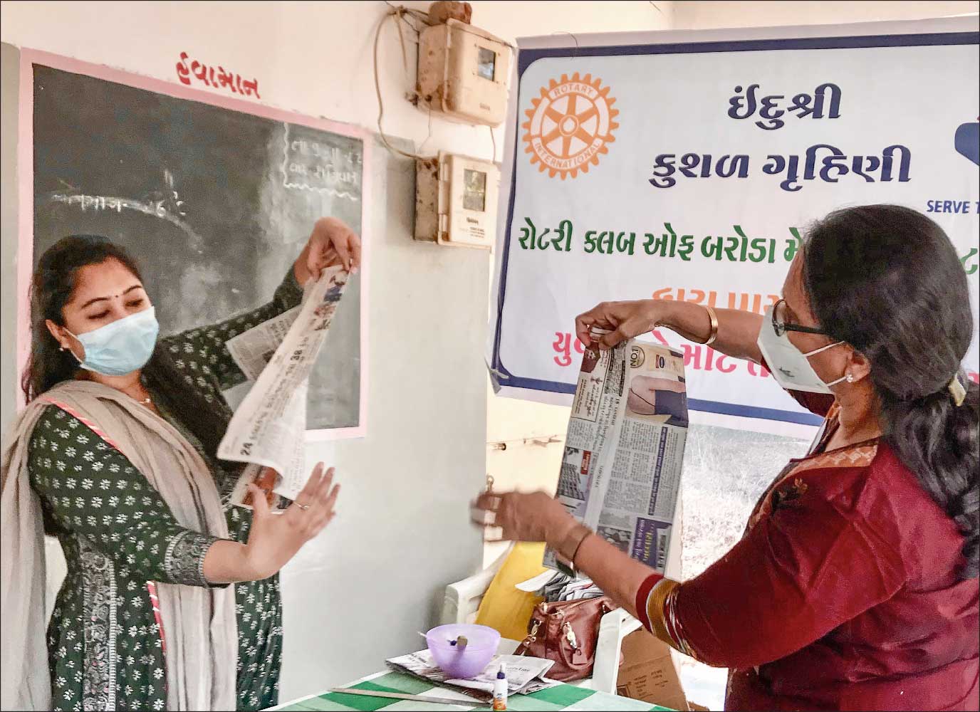 Sharmishtha Desai (R) and Shivangi Parikh demonstrate how to make a paper bag.