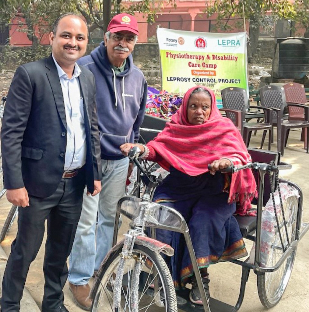 Pawan Tiwari of ACRE and Pradeep Bahri, CEO, Rotary Club Alliance for Leprosy Control, with a woman after presenting a tricycle to her at a disability care camp in RK Puram leprosy colony, Delhi.